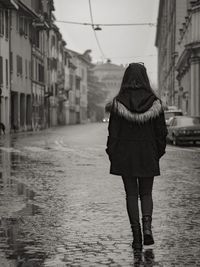 Rear view of woman standing on wet street in rainy season