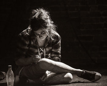 Young woman writing on body with pen while sitting in dark room