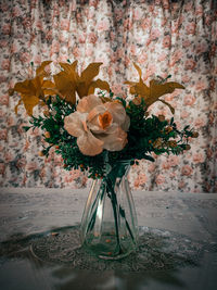 Close-up of rose plant in vase on table against wall