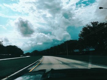 Road against cloudy sky seen through car windshield