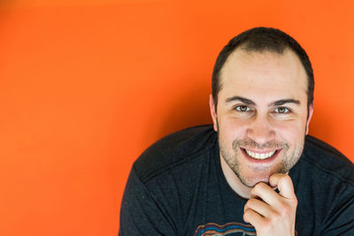 Portrait of smiling mid adult man with hand on chin against orange wall