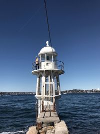 Man standing on lighthouse against clear blue sky