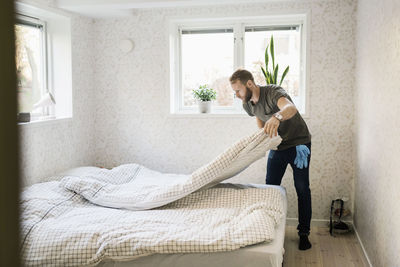 Full length of man making bed in house