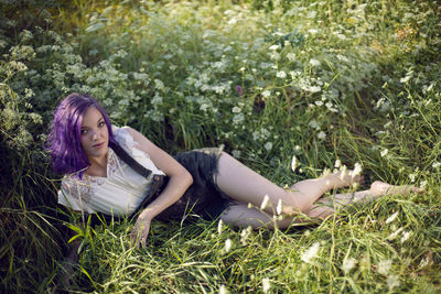 Portrait of a teenage girl with purple hair and an earring in her nose lying in the grass in nature