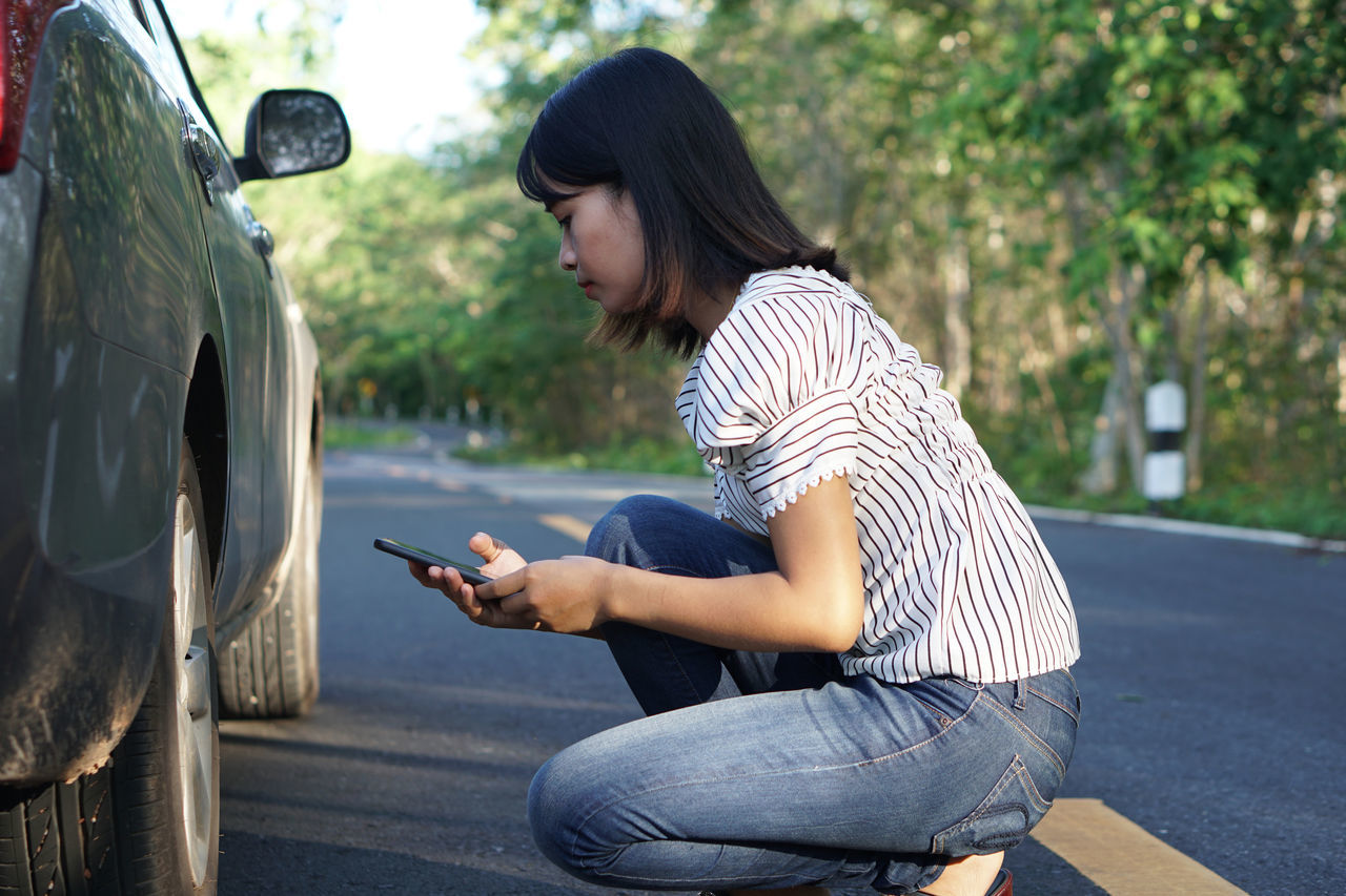 FULL LENGTH OF MAN USING MOBILE PHONE WHILE SITTING ON CAR