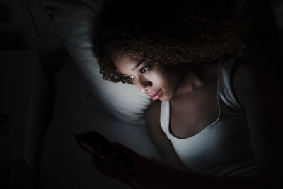 Woman using smart phone while lying on bed in dark room at home