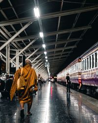 Rear view of people walking on illuminated railroad station platform