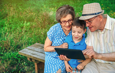 Grandparents and grandson looking at digital tablet while sitting on bench in park