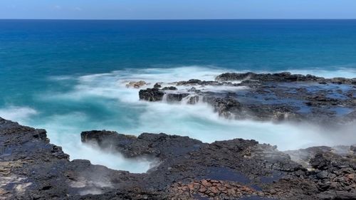 Scenic view of waves breaking on rocks at shore against sky