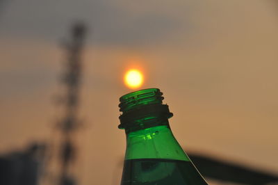 Close-up of glass bottle against sky during sunset