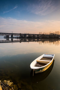 Boat moored on river against sky during sunset