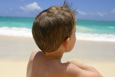 Rear view of shirtless boy sitting at beach