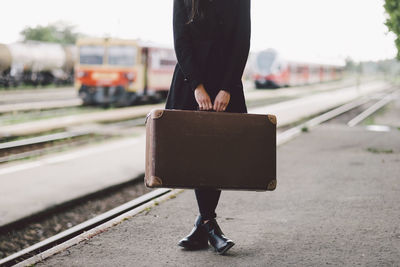 Low section of woman carrying suitcase while standing on railroad station platform