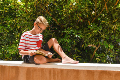 Full length of boy reading book while sitting on building terrace
