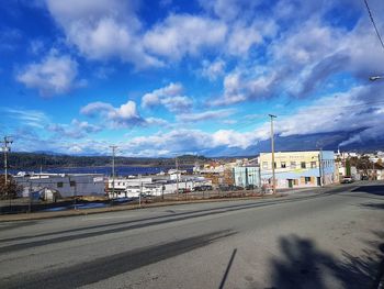 Road by buildings against blue sky