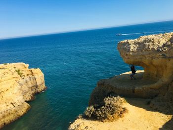 High angle view of woman with arms raised standing on rock formation by sea