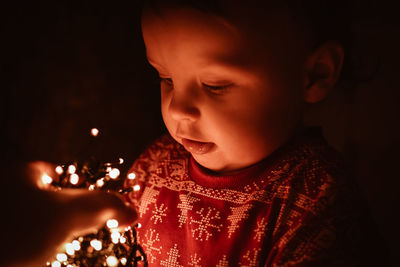 Close-up of cute girl looking at string lights in darkroom