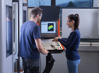 Engineer assisting trainee standing near cnc machine at factory