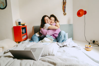 Happy young female friends embracing while sitting at home