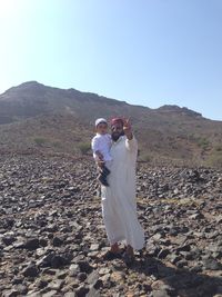 Couple standing on mountain against clear sky