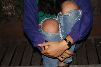 Midsection of woman wearing torn jeans while hugging knees